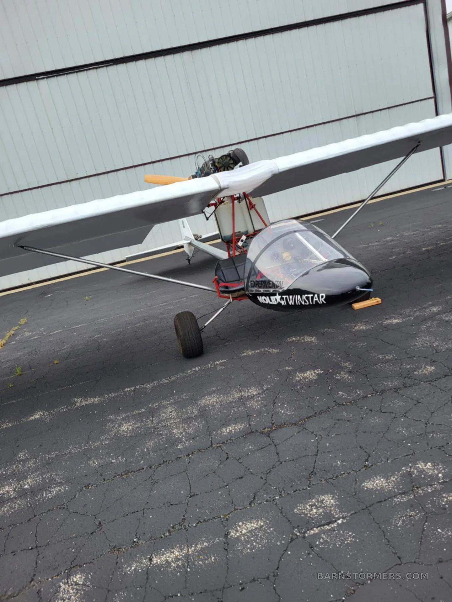 A black and white Volmer VJ-24W SunFun experimental aircraft is parked on an asphalt ramp next to a hangar.