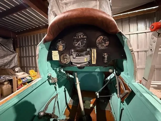 The cockpit of a vintage aircraft with a brown padded coaming and a black instrument panel with several gauges.