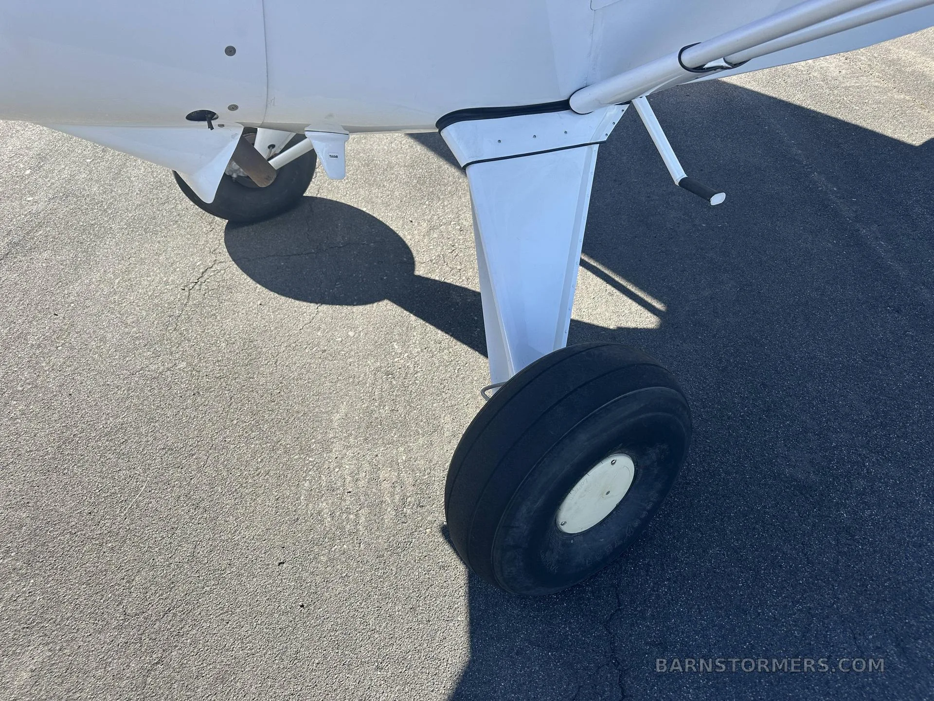 A close-up view of the main landing gear and tire of a white Maule M-7-235 aircraft, showing the wheel hub.
