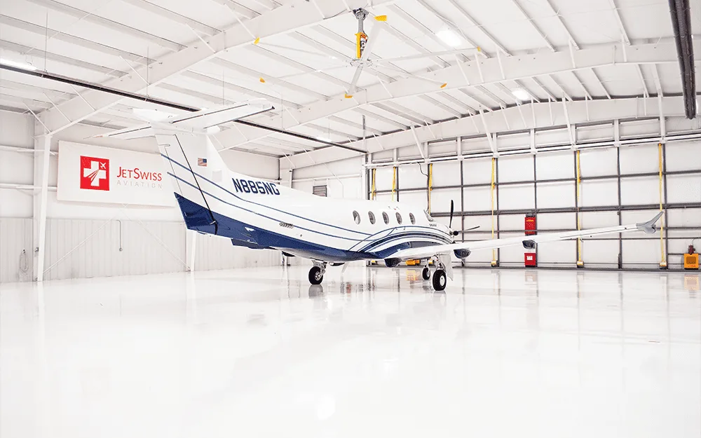 A white and blue Pilatus PC-12 aircraft, tail number N885NG, is parked in a brightly lit hangar.