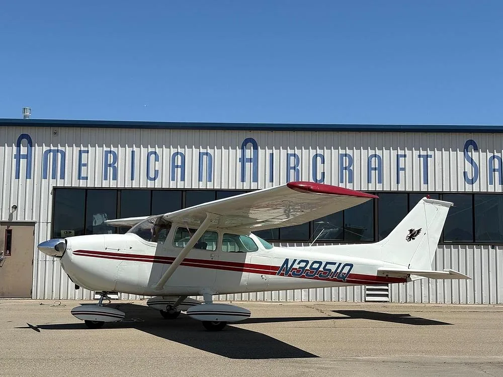 A white Cessna aircraft with red stripes and N3951Q registration parked in front of the American Aircraft building.