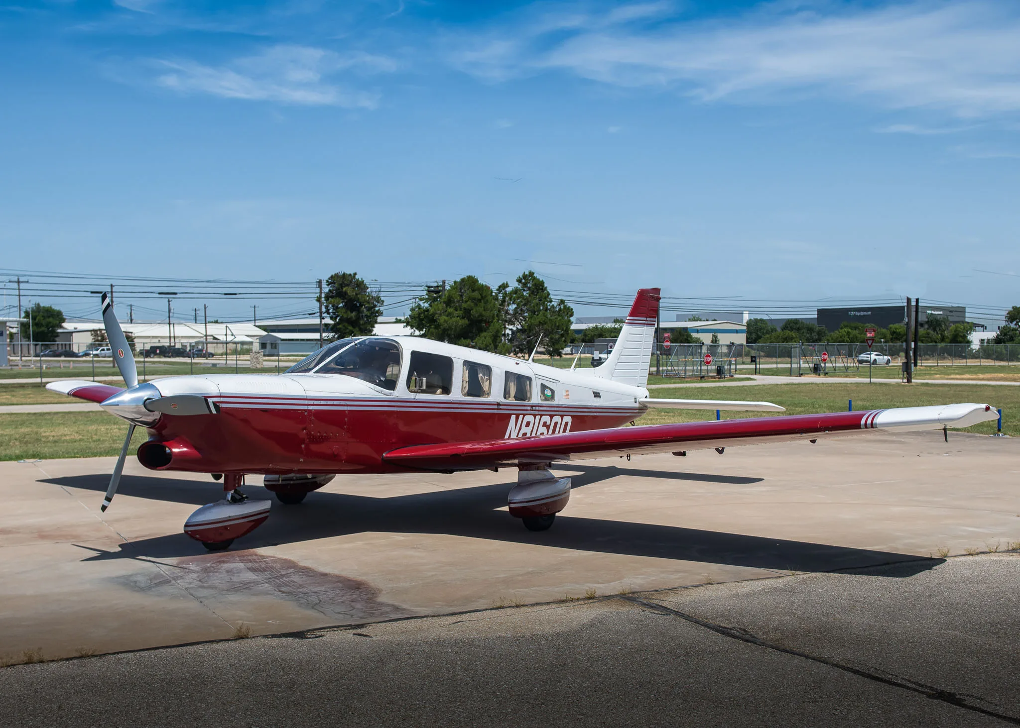 A red and white Piper Cherokee aircraft, N8160D, parked on an airport tarmac.