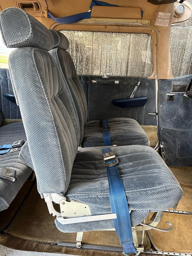 The blue fabric front and rear seats of an aircraft cabin, viewed from the side, with a sunshade on the window.