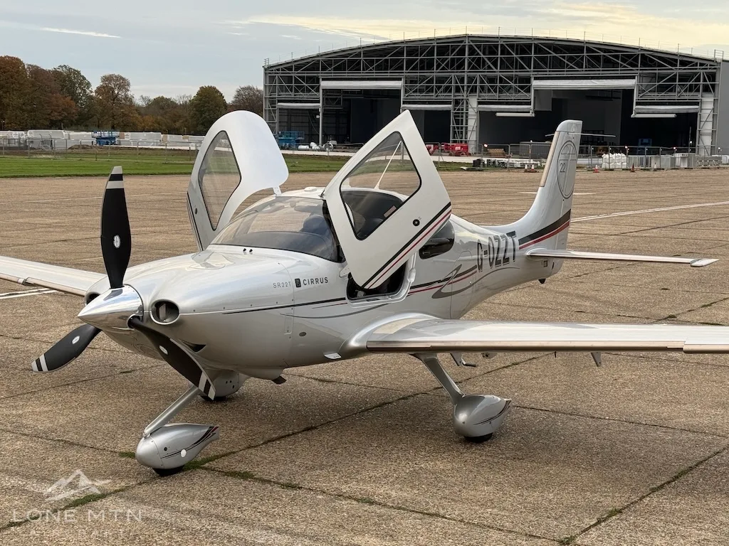 A silver Cirrus SR22T aircraft with open doors parked on an airfield tarmac.