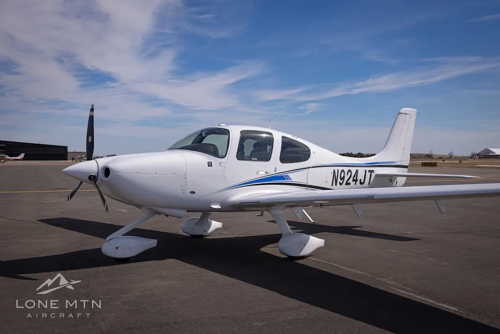 A white single-engine aircraft with blue and black stripes, tail number N924JT, parked on an airport tarmac under a blue sky.