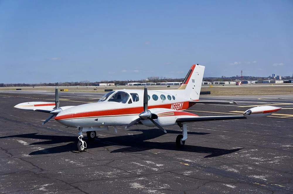 A white and red Cessna 400 series twin-engine aircraft, registration N555MY, is parked on an asphalt tarmac under a clear blue sky, viewed from the front-left.