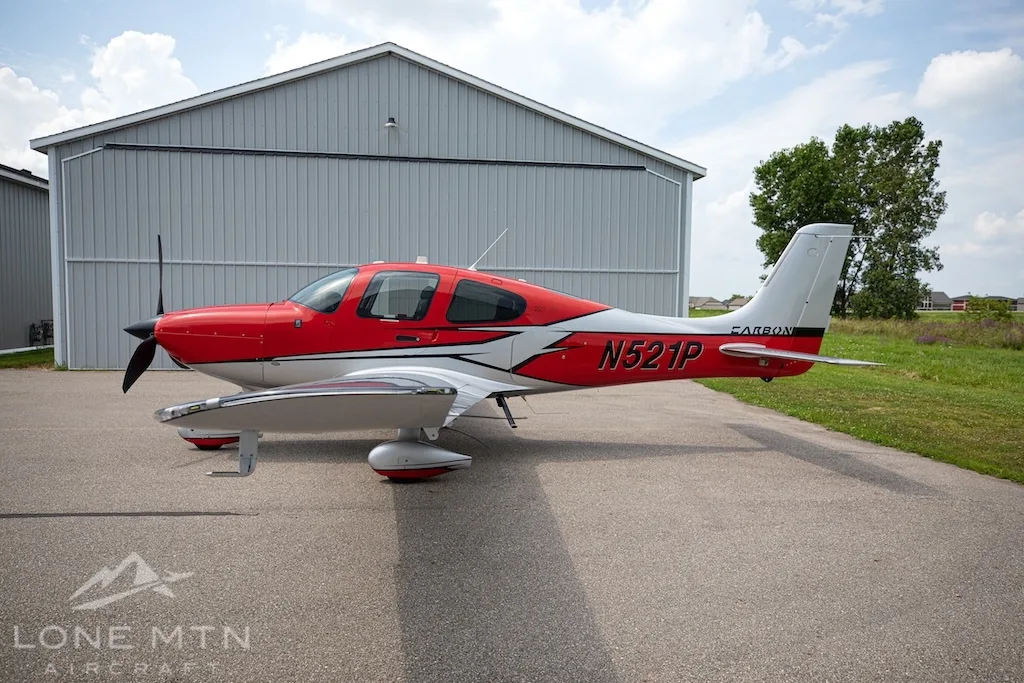 A red and silver Cirrus SR22 aircraft, N521P, parked on an asphalt ramp in front of a hangar.