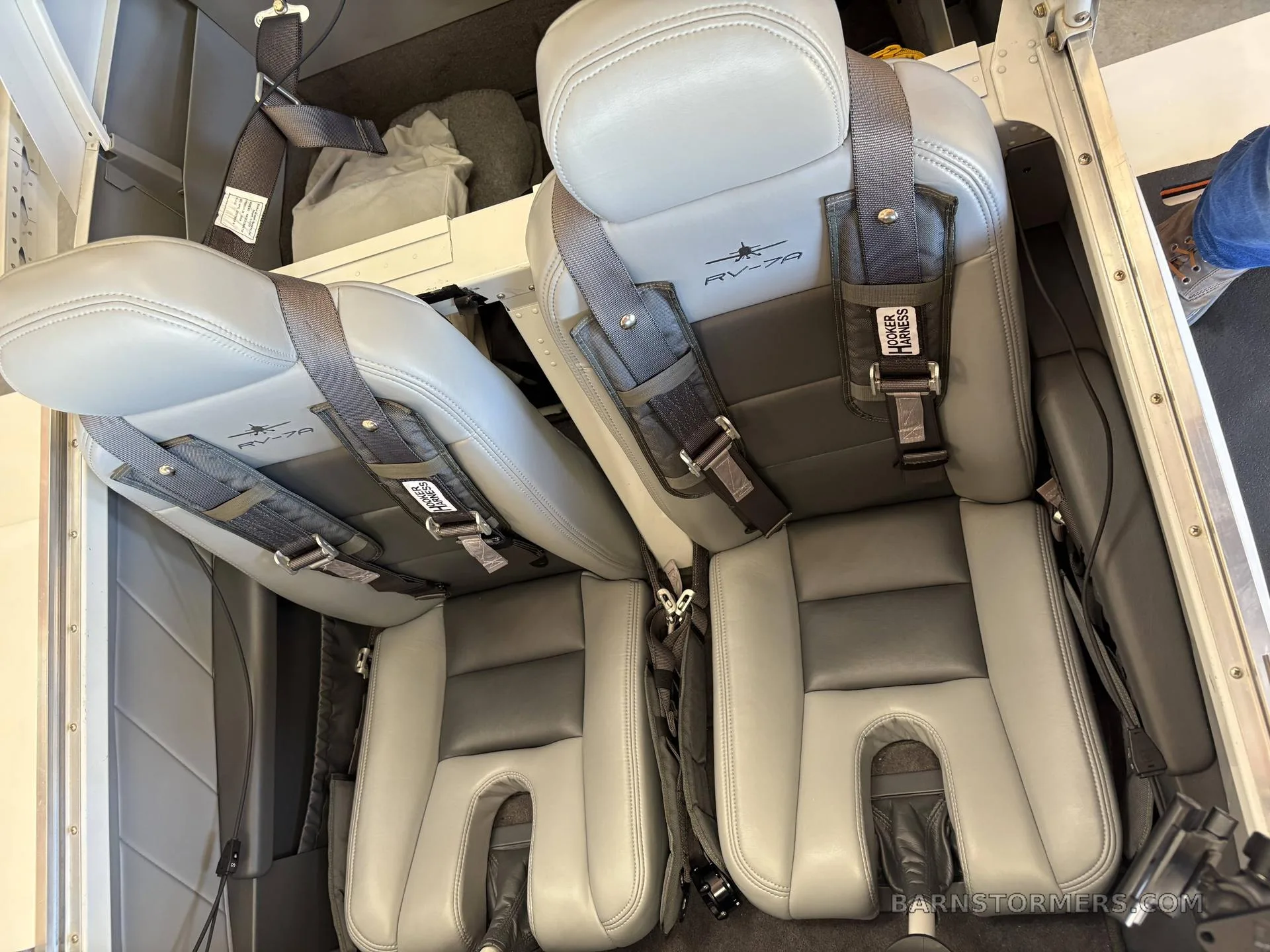The gray leather two-seat interior of a Vans RV-7 aircraft with harnesses.