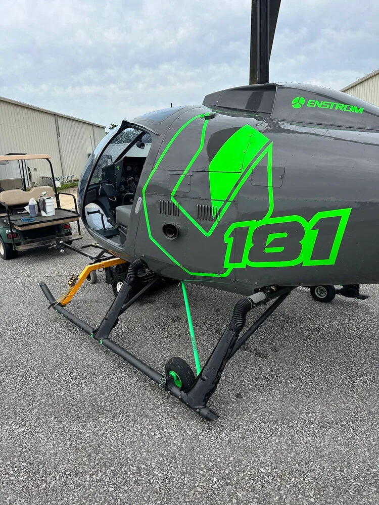 A close-up of the right side of the gray Enstrom helicopter N88ZH, showing the green "181" graphic and "ENSTROM" logo.