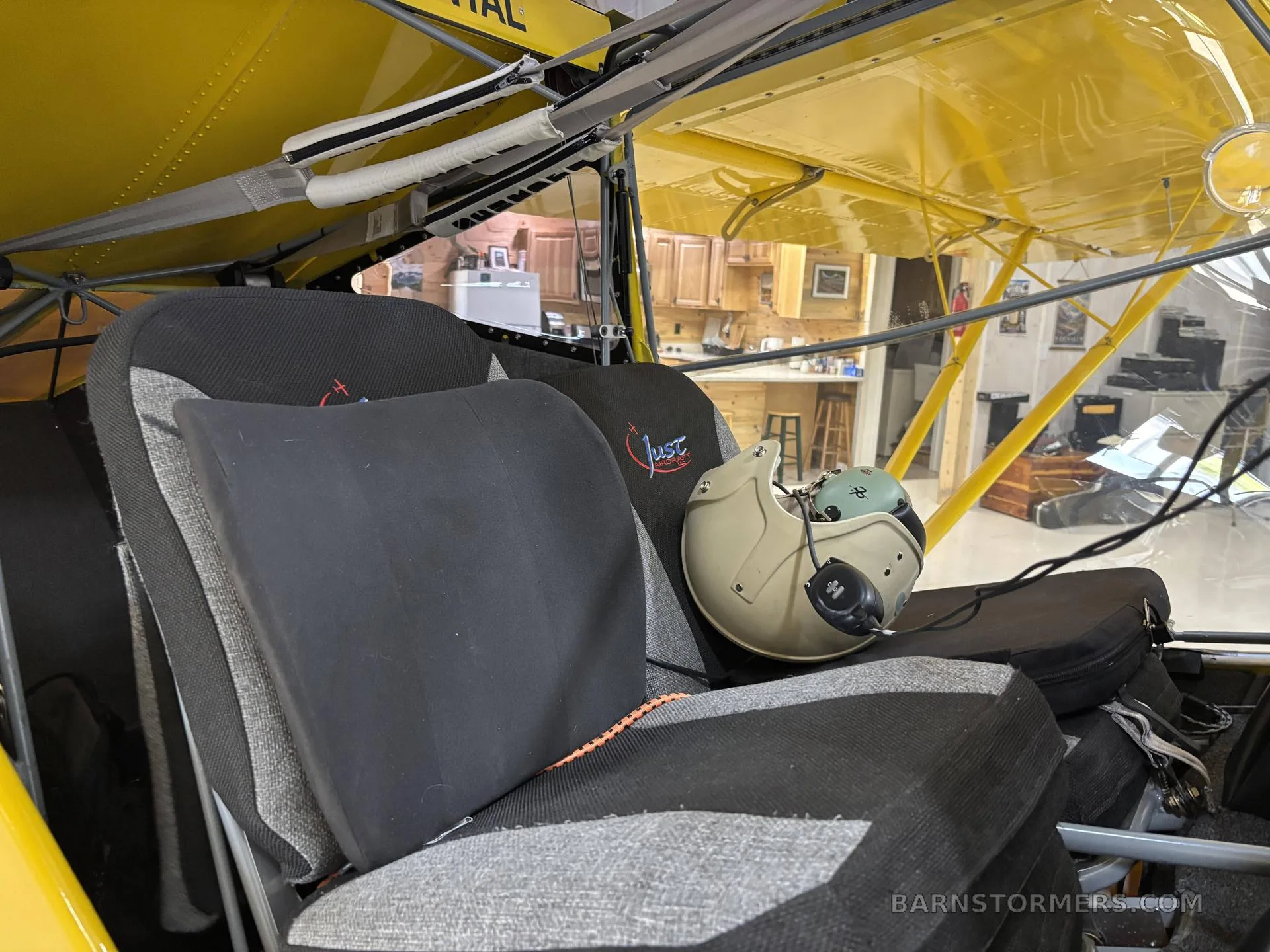 The gray and black fabric seats of a small aircraft, with a flight helmet resting on the right seat.