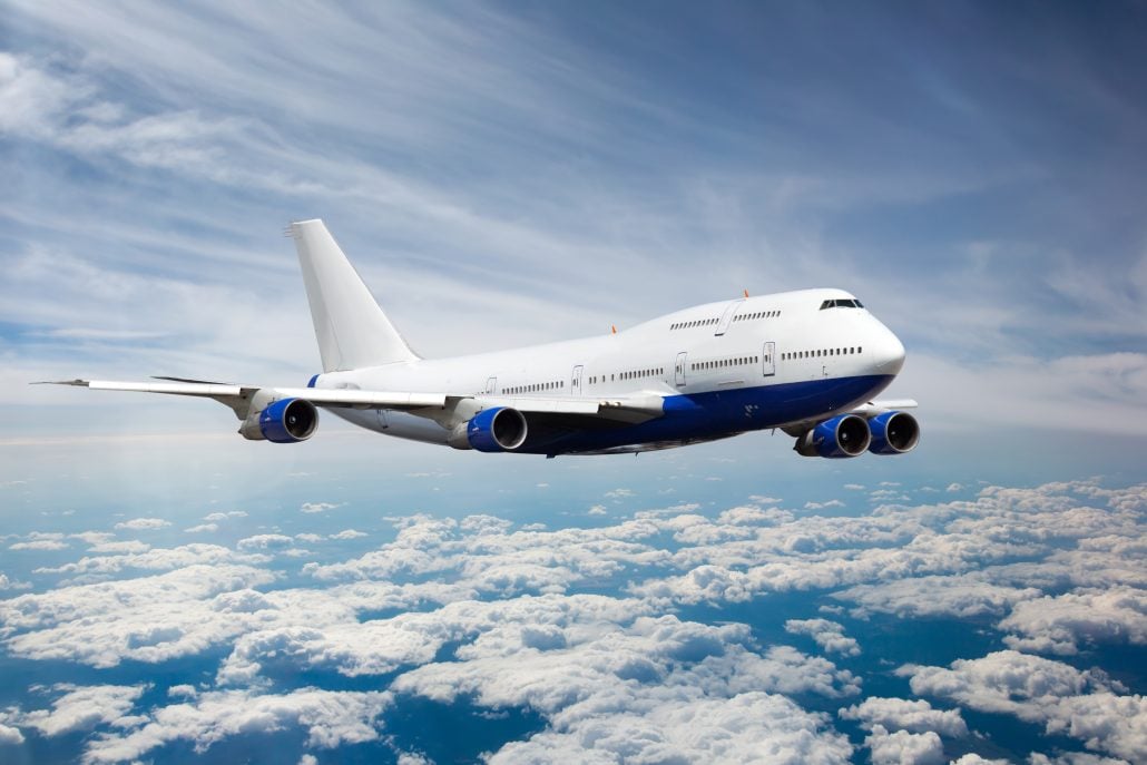 A large white and blue Boeing 747 aircraft flying above a scattered cloud layer.