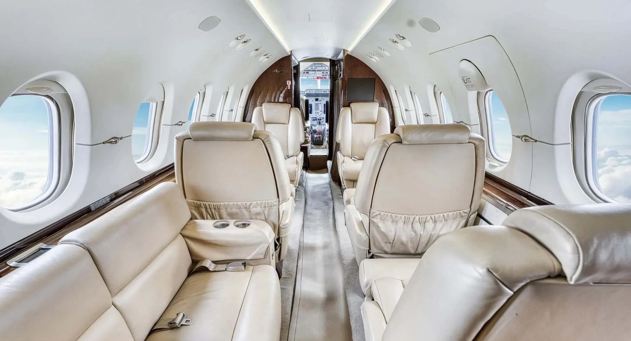A spacious view of the private jet cabin interior with light beige leather seating and a rear galley.