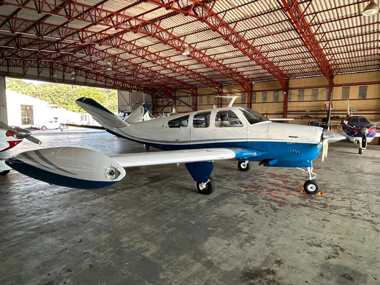 A white and blue single-engine propeller aircraft is parked in a hangar with other planes.
