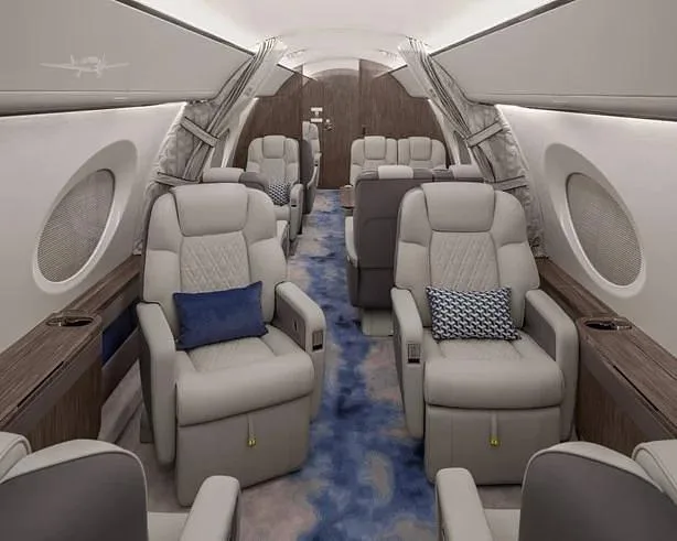 The luxurious interior cabin of a private jet features light grey quilted leather seats and a blue patterned carpet.