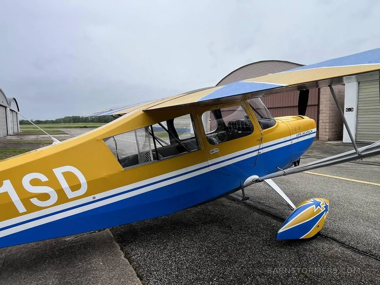 A close-up side view of the yellow and blue Super Decathlon aircraft with tail number N71SD, showing the cabin and landing gear.