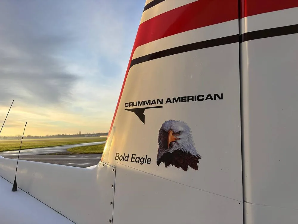 A close-up of the tail of the Grumman American aircraft, showing "Grumman American" text and a "Bold Eagle" graphic.