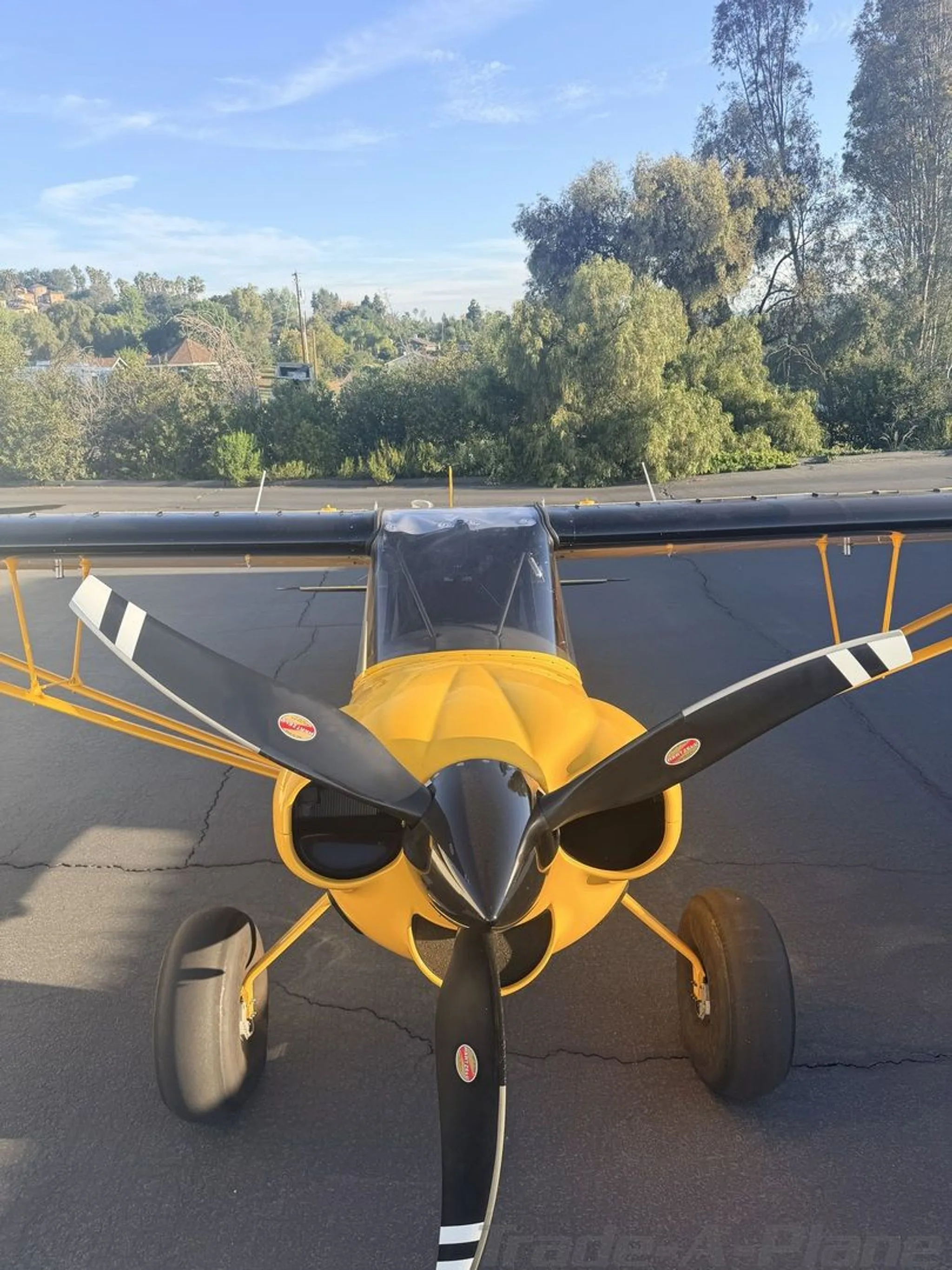 A head-on view of the yellow CubCrafters XCub, showing its propeller and large tires, parked on an asphalt tarmac.