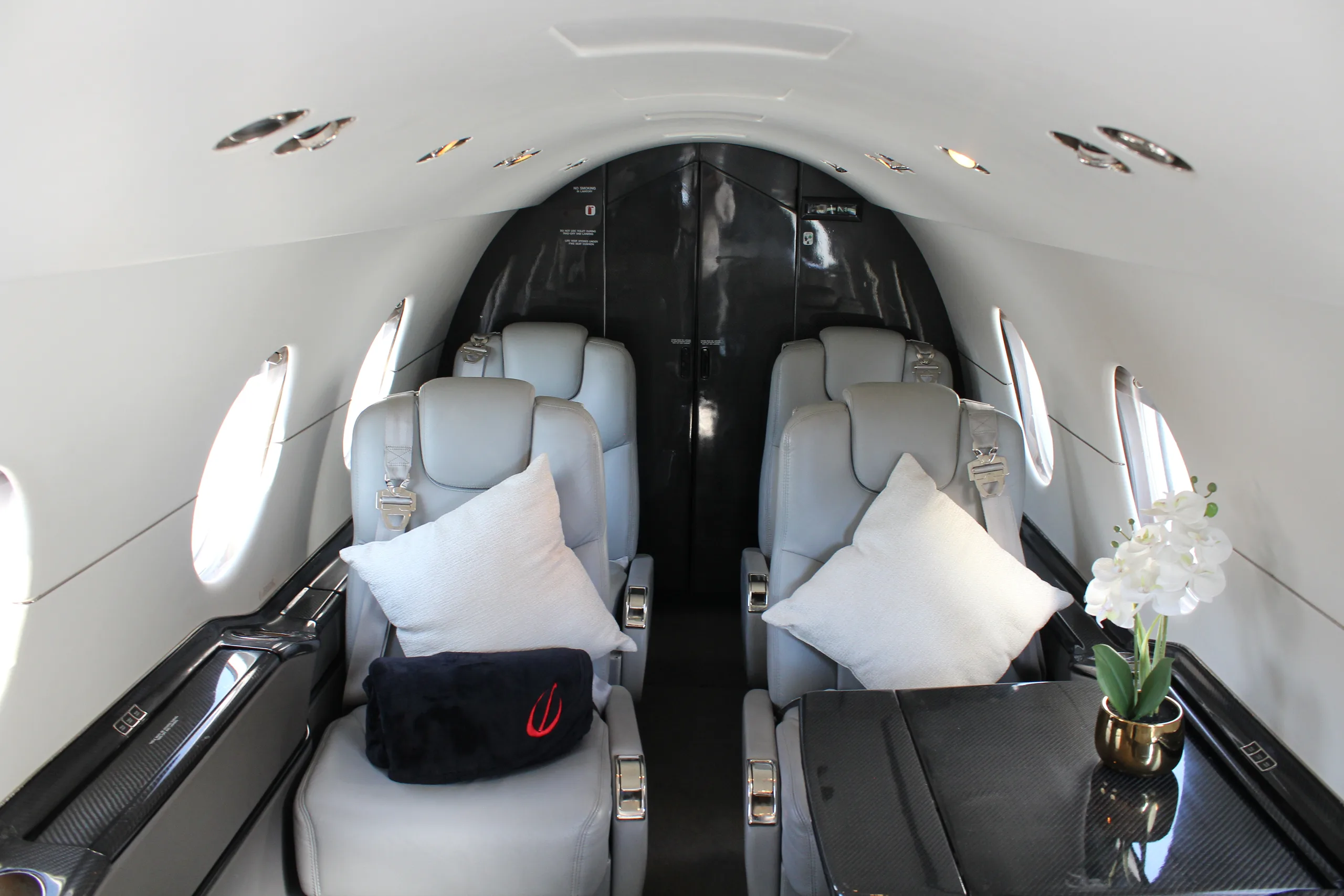 A view of the aircraft cabin showing gray leather seats and a small table with a flower arrangement.