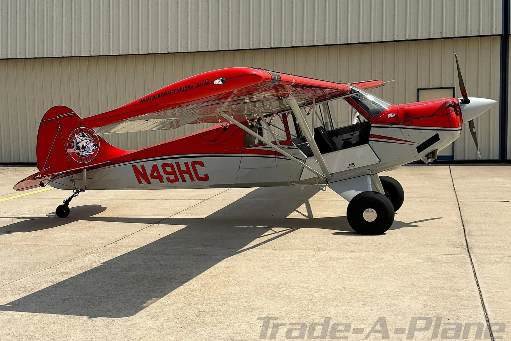 A side view of the red and white Aviat Husky A-1C aircraft, registration N49HC, parked on an airfield.