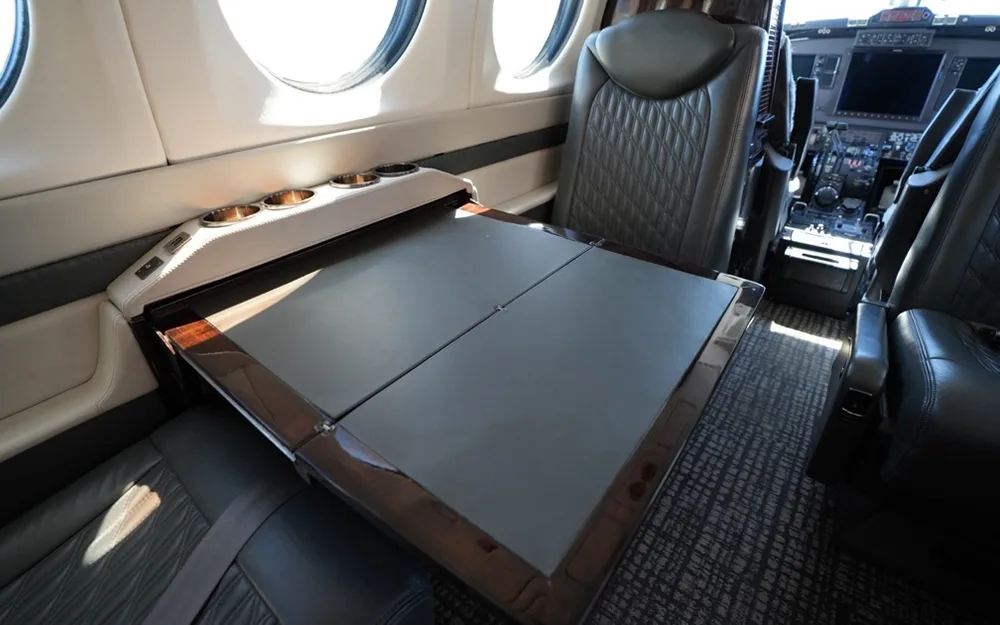 A view inside the aircraft cabin showing a folded-out table with cup holders and a grey quilted leather seat.