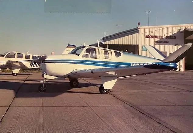 A white single-engine aircraft with blue stripes parked on a tarmac in front of a hangar at Mondell Field.