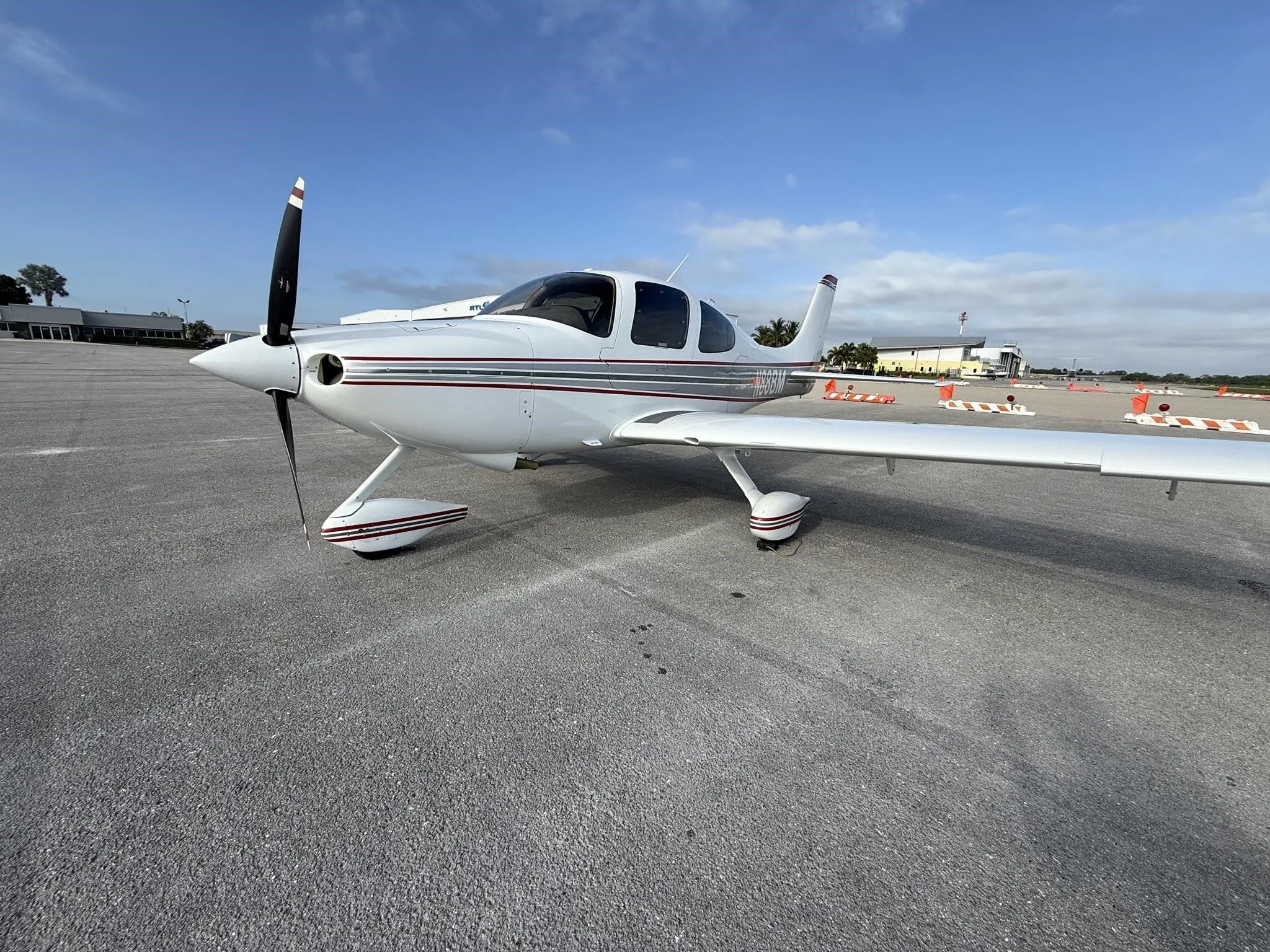 A front-left view of a white Cirrus SR22 aircraft with red and gray stripes, tail number N88BM, parked on an airport tarmac.