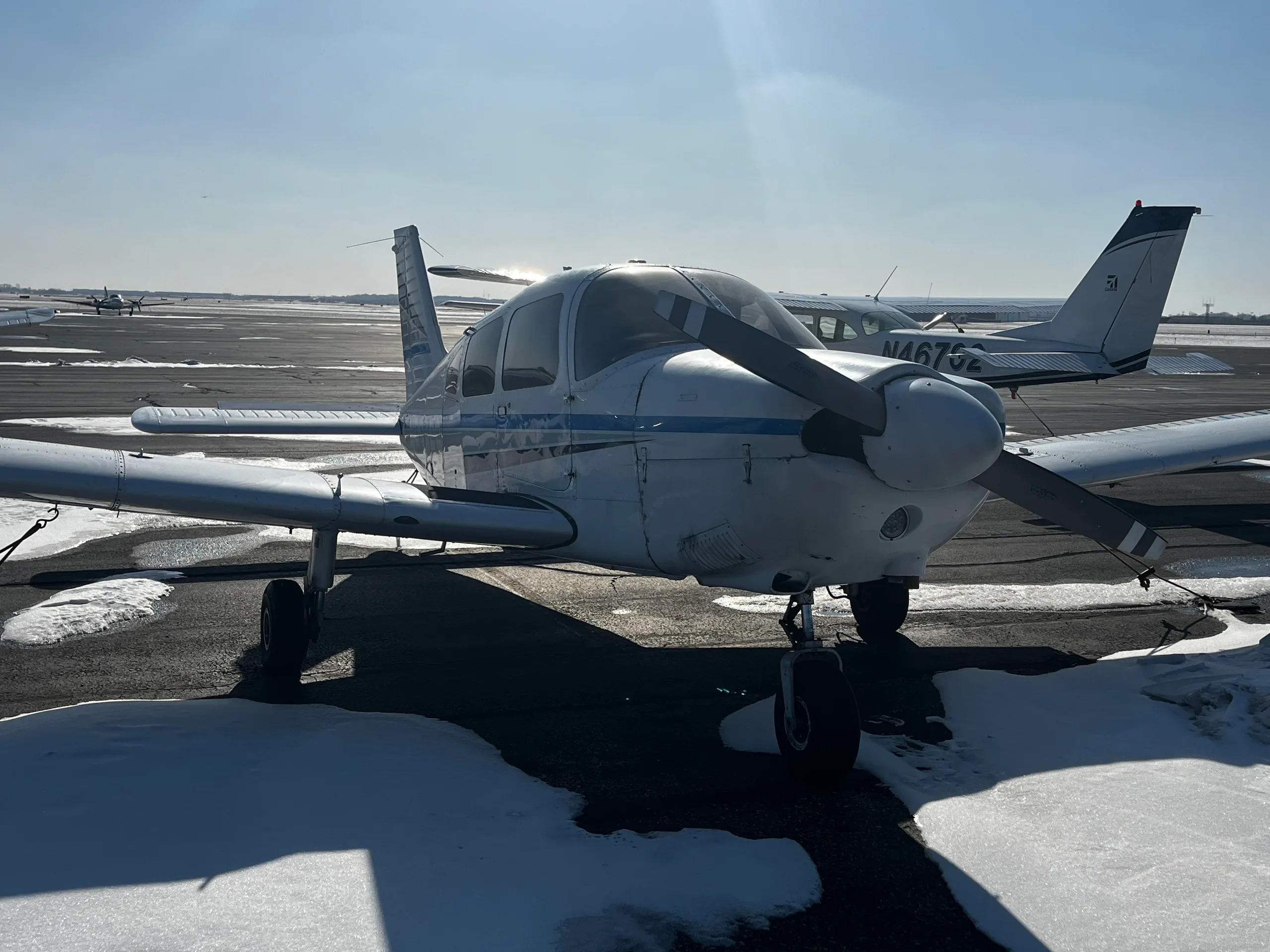 Front view of a white single-engine propeller aircraft with blue and grey stripes on a snowy tarmac.