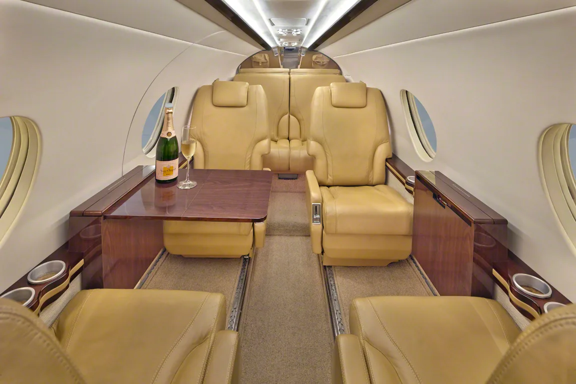 Interior view of the aircraft cabin with tan leather seats, table, champagne and glass.
