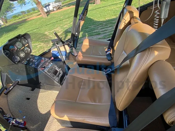 The interior of a helicopter features tan leather seats, seatbelts, and a view of the cockpit instruments.