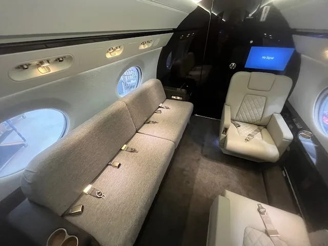 A view of the business jet cabin interior featuring a long light-colored sofa and a single seat.