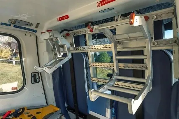 The interior of a helicopter cabin shows medical stretcher mounts and blue seats.
