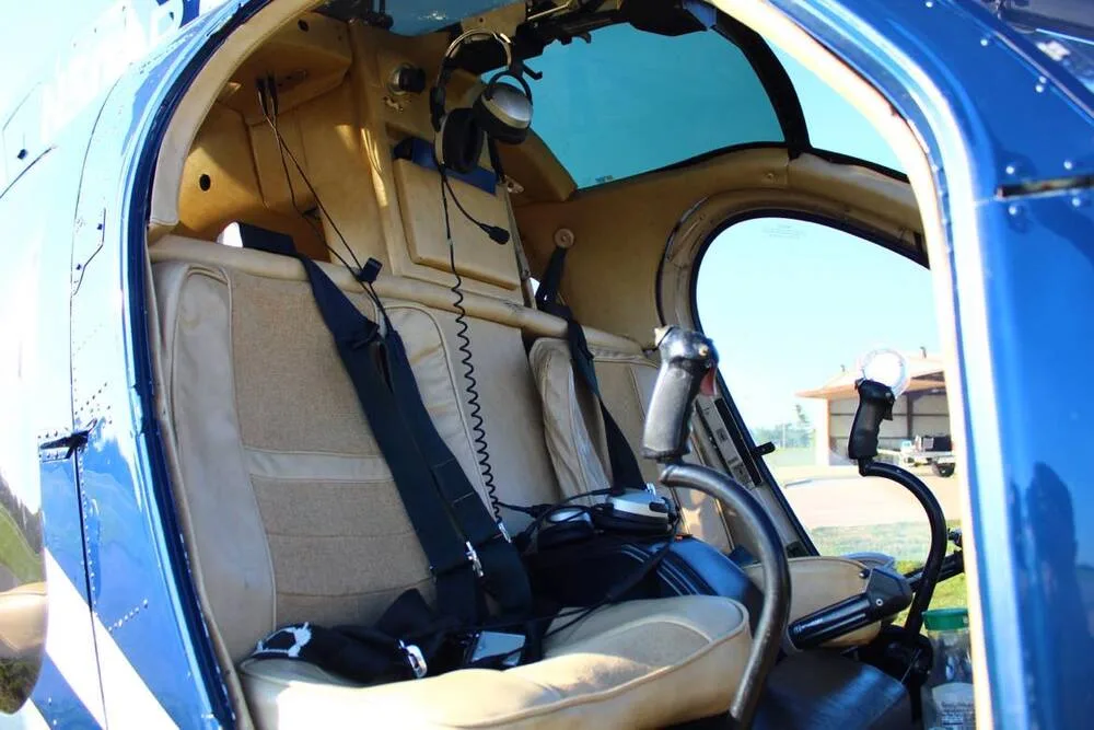 The cockpit interior of a helicopter shows tan seats, flight controls, and headsets.
