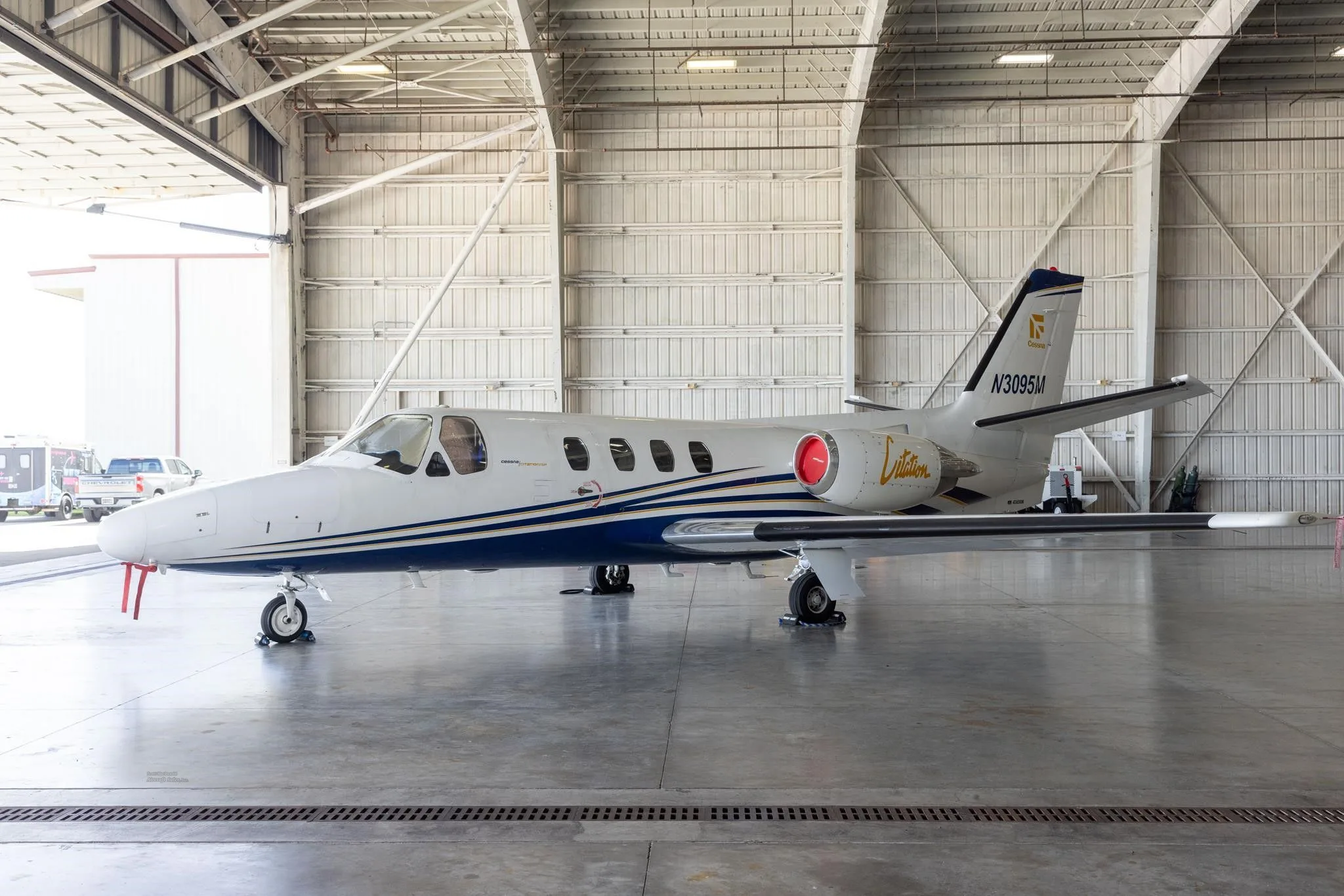 A side view of the white and blue Cessna Citation jet (N3095M) parked inside a hangar.