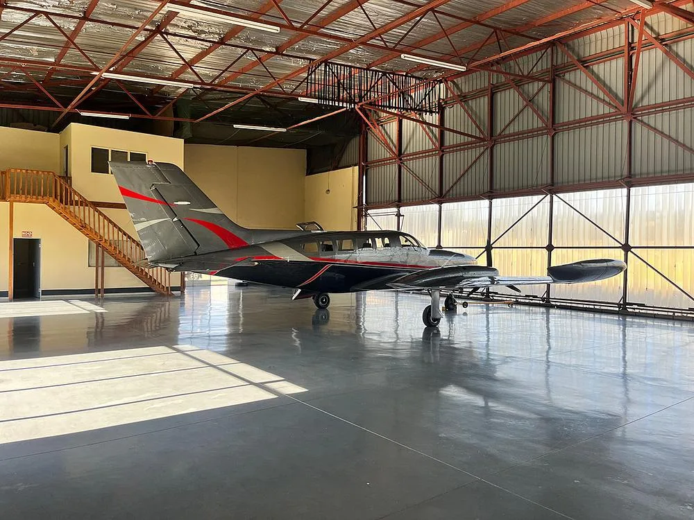 A dark grey twin-engine aircraft with red and silver accents, viewed from the rear-right in a hangar.