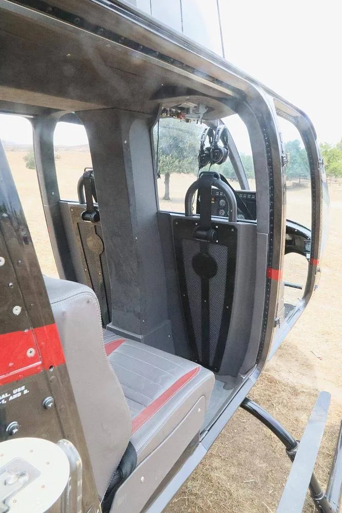 The helicopter interior shows the grey and red front seats and the cockpit area from a rear-facing perspective.