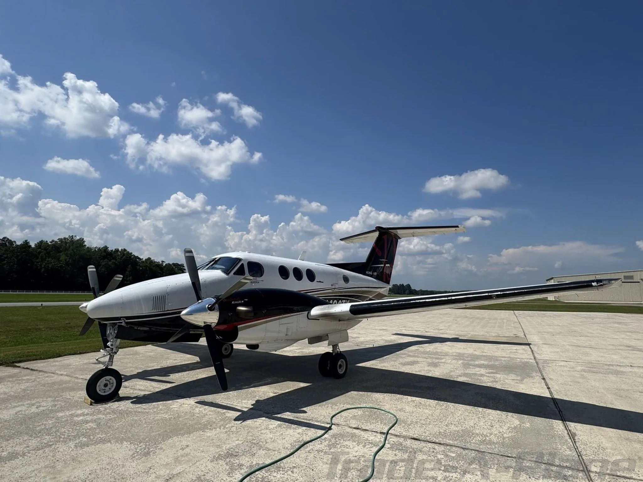 A white and black Beechcraft King Air F90 with red accents on the tail, N490TX, parked on a concrete tarmac under a blue sky.