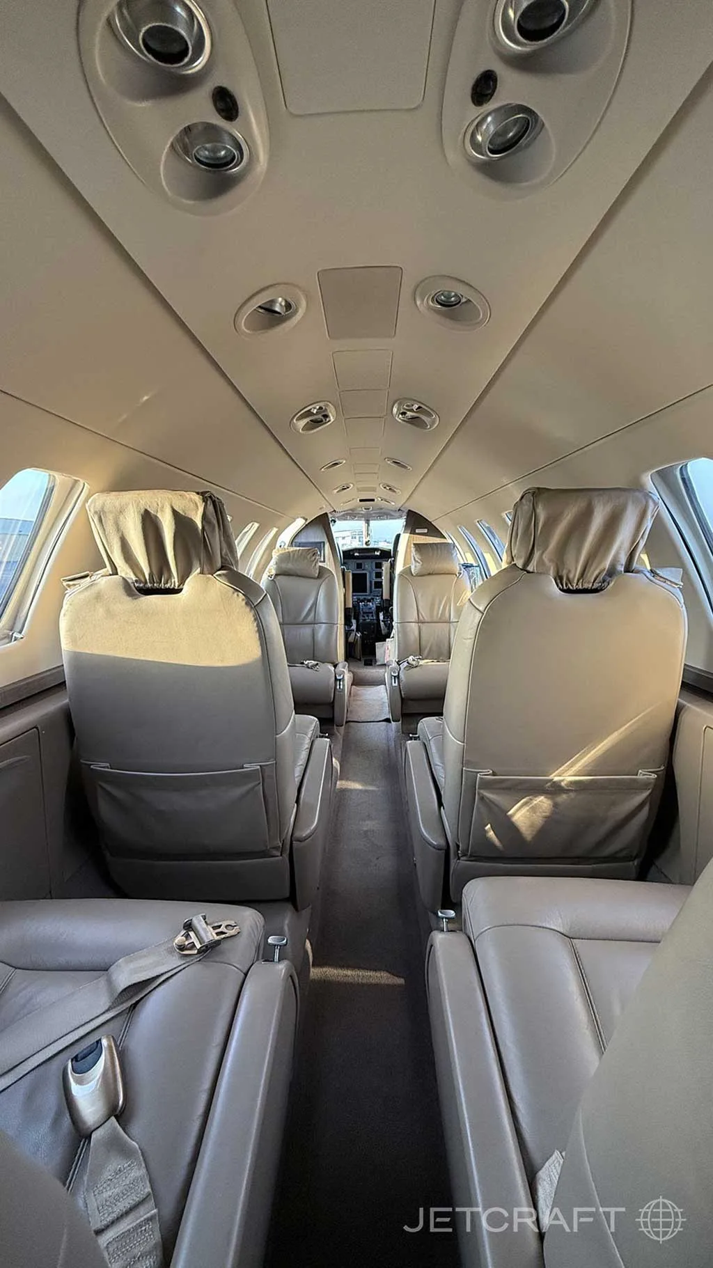 The interior of a business jet cabin with light tan leather seats, viewed from the rear looking forward.