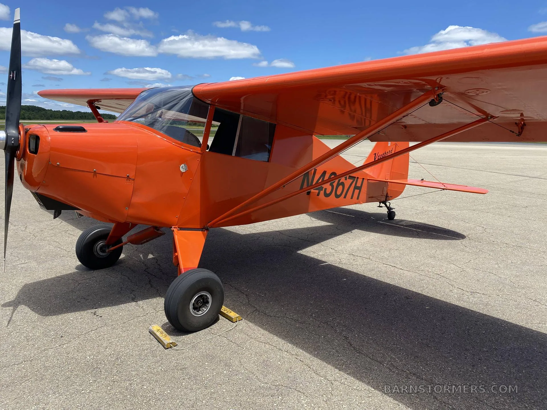 An orange single-engine aircraft with its door open, revealing a blue seat and the instrument panel.