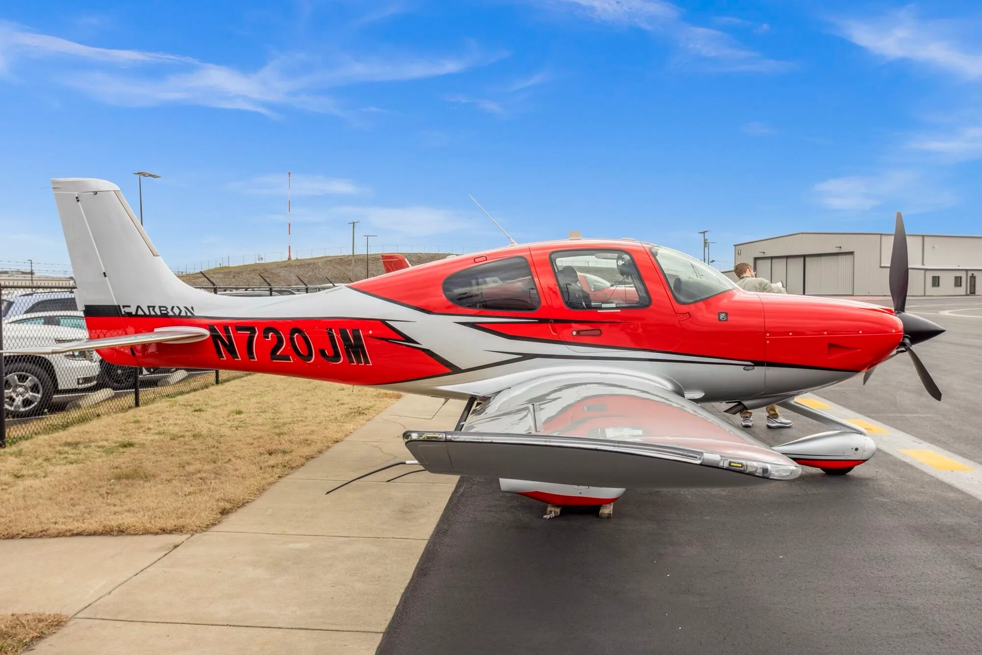 A red and silver Cirrus SR22 aircraft with registration N720JM parked on an airport tarmac.