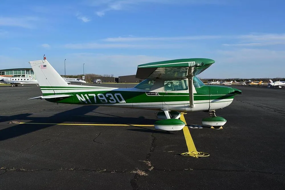 A three-quarter rear view of a green and white Cessna 172 aircraft, registration N1793Q, on an airport ramp with other planes.