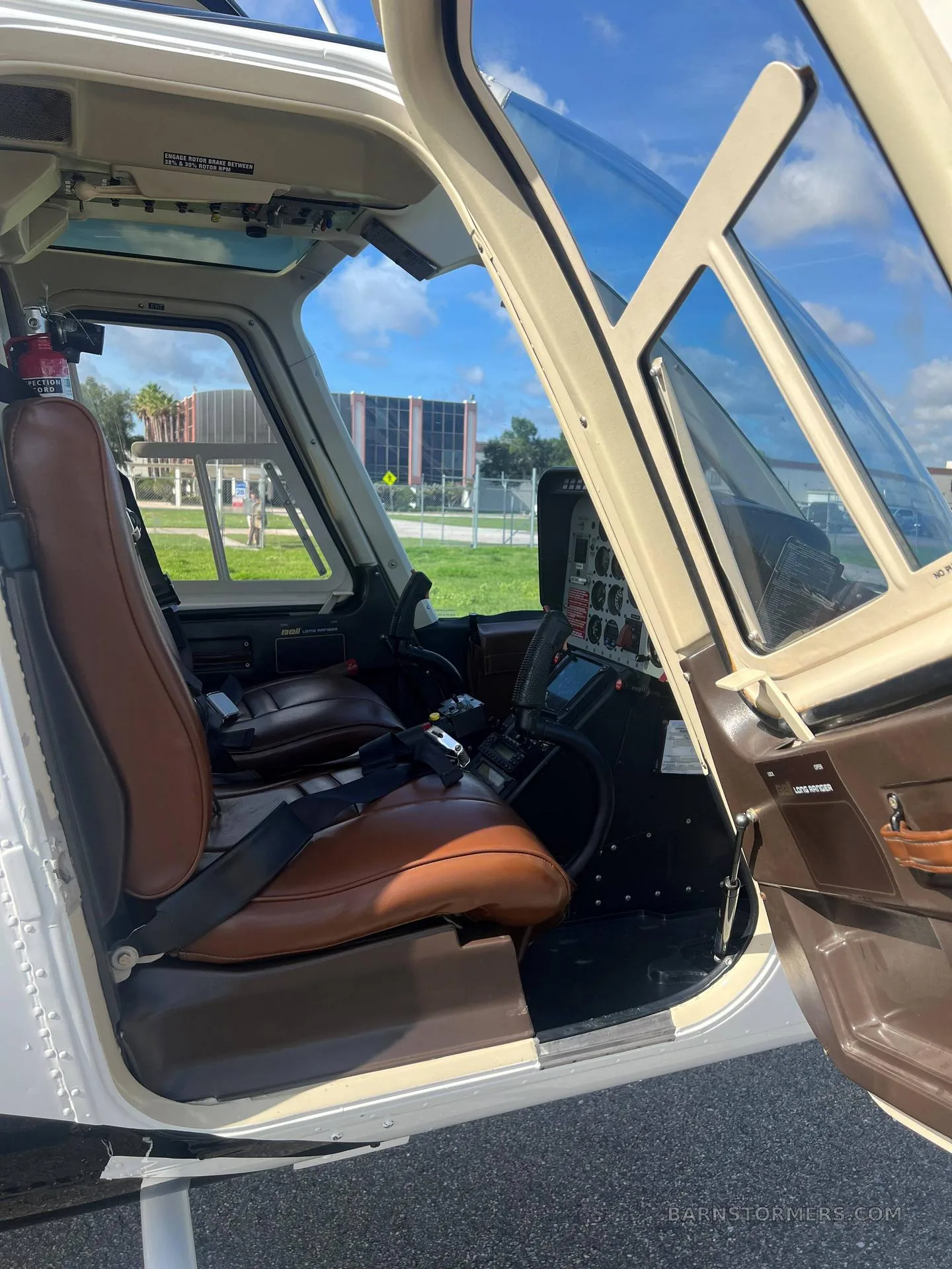 The brown leather interior and cockpit of a Bell 206 helicopter are visible through the open doors.