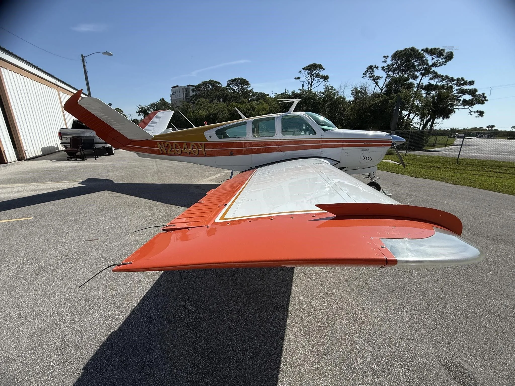 The left wing and tail of a white and orange single-engine aircraft, N2040Y, parked on an asphalt ramp.