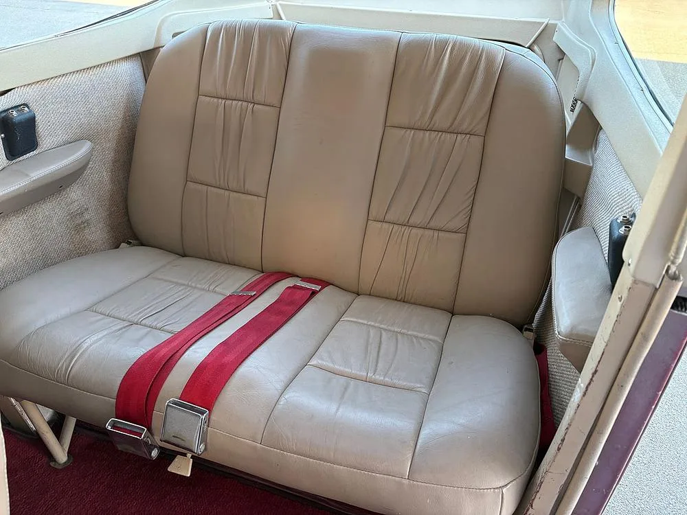 The tan leather rear bench seat with red seatbelts in the aircraft cabin.