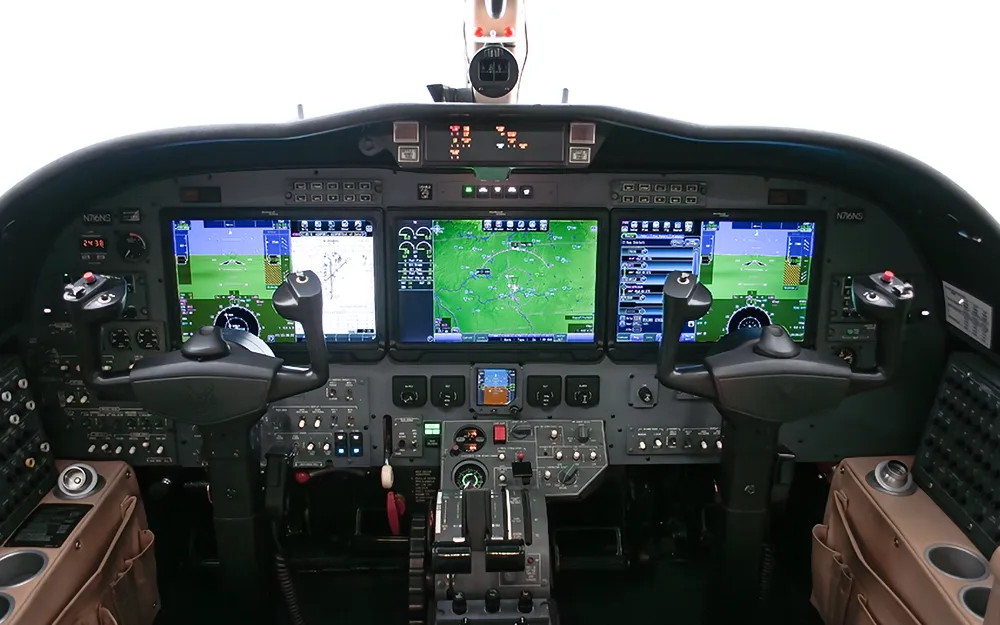 The cockpit of a modern business jet, featuring multiple large digital displays showing navigation and flight information.