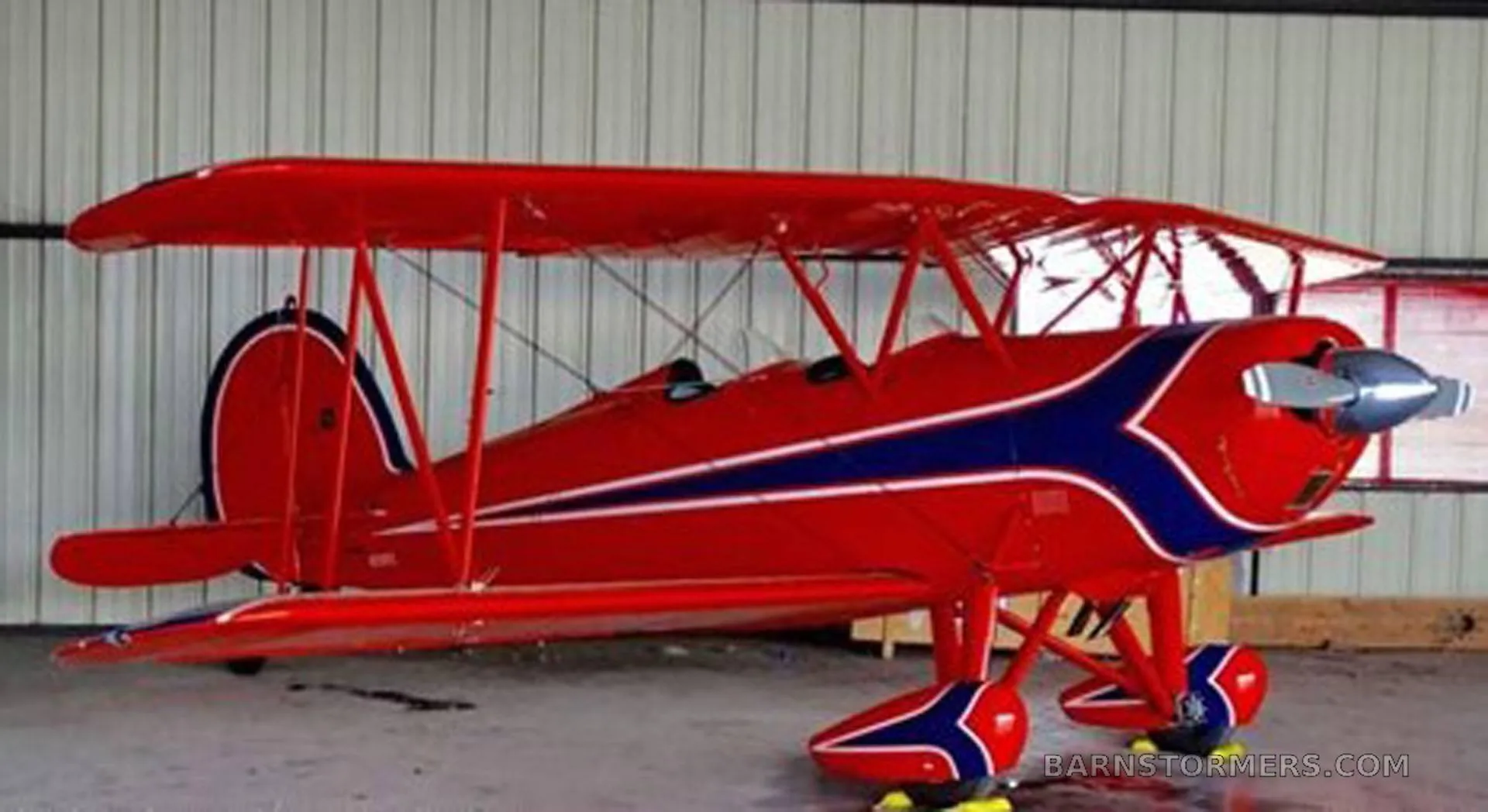 A red biplane with blue and white stripes is parked inside a hangar.