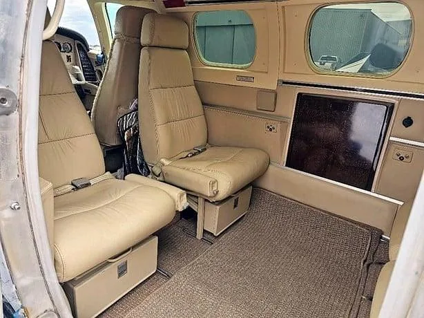 The aircraft cabin interior with two tan leather passenger seats and a carpeted floor.