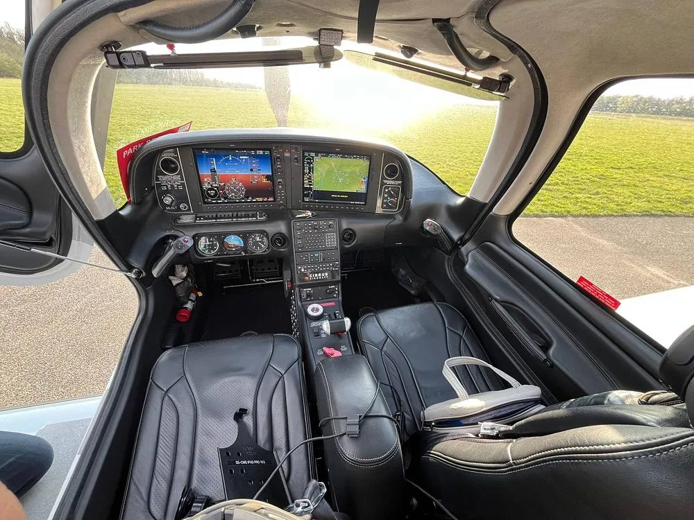 The cockpit of a Cirrus SR22T aircraft, showing the instrument panel with two large displays and black leather seats.