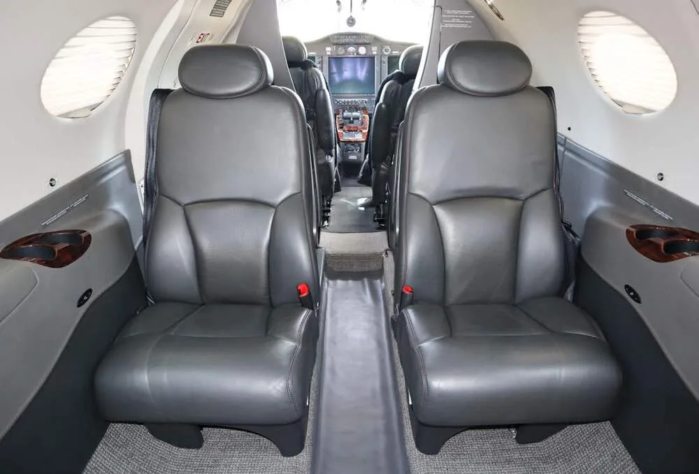 View of the aircraft's cabin interior with two rows of dark gray leather seats and a view into the cockpit.