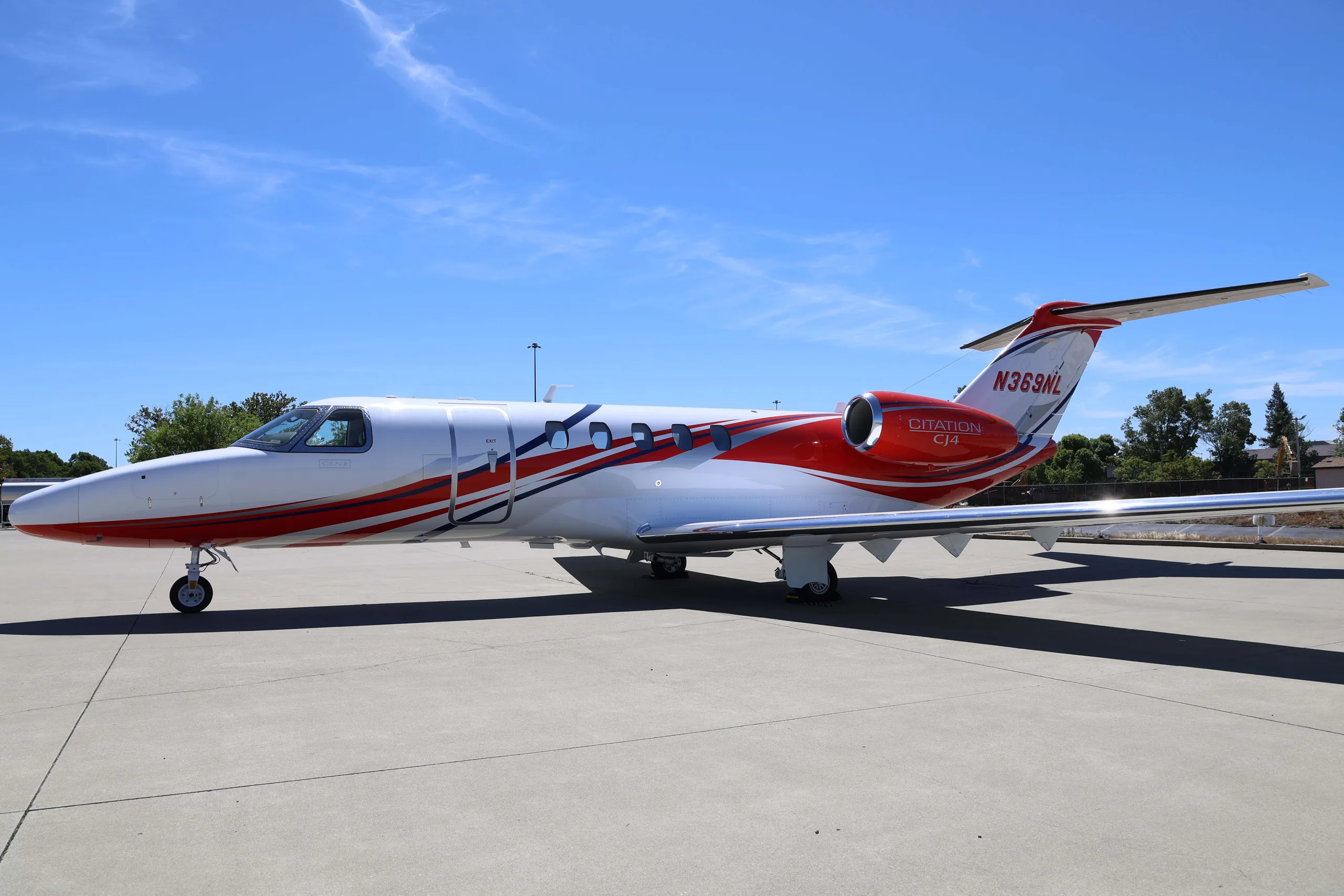 A side view of the white Cessna Citation CJ4 (N369NL) with red and blue stripes, parked on an airfield.