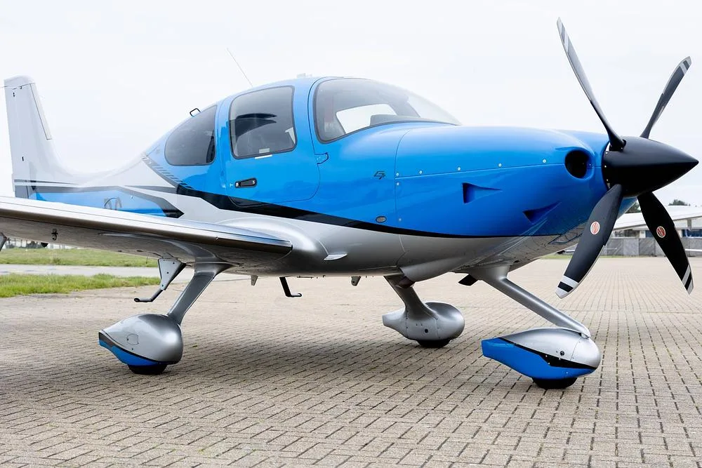 A close-up, low-angle view of the front and side of a blue and silver Cirrus SR22T GTS aircraft.